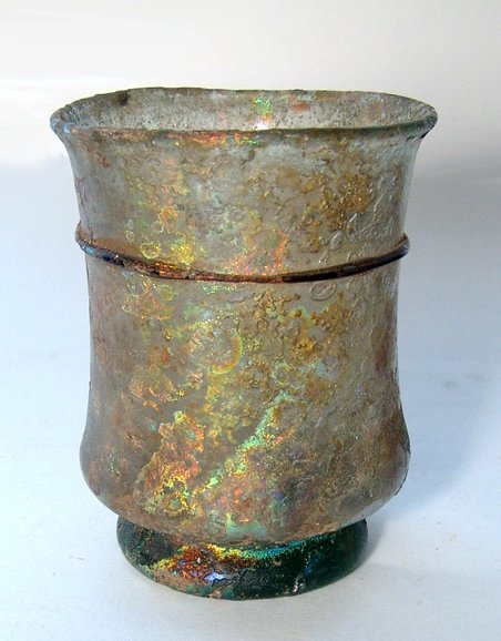 Roman glass beaker with beautiful iridescence: A Roman pale green glass beaker with beautiful iridescence, c. 4th Century AD, on wide foot pad formed with the rest of the vessel. The sides are wider near the foot than flare at the mouth, above a s