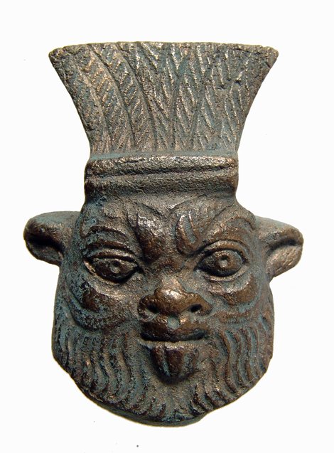 Detailed bronze face of Bes from Egypt: A detailed bronze face of Bes, Late Period, c. 664 - 343 BC, with four notches on the sides indicating it was part of a larger element, perhaps a mirror. H: 2 3/8" (6.1 cm). Intact with nice brown sur