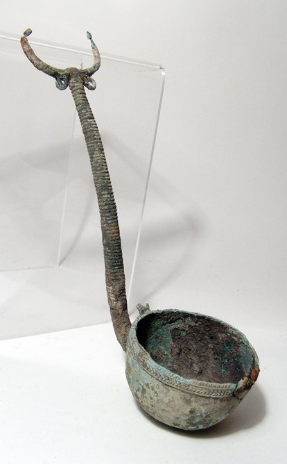 Central Asian bronze ladle, c. 1st Millennium BC: A Central Asian bronze ladle, c. 1st Millennium BC, with hemispherical bowl with decoration around the rim, the handle adorned with ridges and topped by a pair of horns, loops on either side below. L: