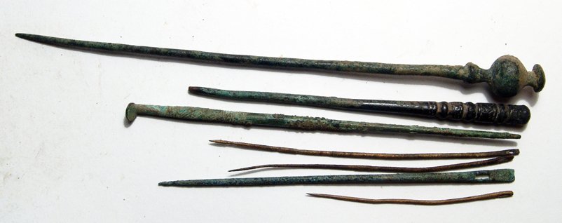 A Lot of 7 Roman & Near Eastern Implements: A lot of 7 Roman bronze implements, c. 1st - 3rd Century AD. Lot includes a stylus with nicely incised handle, a probe with angled end and incised decoration, and four needles with small rectangular h