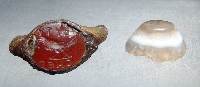 A pair of Roman ring stones: A pair of Roman ring stones, c. 1st - 3rd Century AD, the first is a carnelian stone still set within the iron ring, the lightly domed top incised with an eagle standing to lt. with a wreath in its be