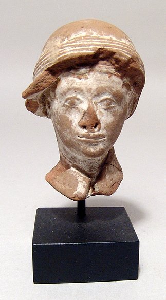 A Hellenistic terracotta head of a man: A Hellenistic terracotta head of a man, c. 3rd - 2nd Century BC, wearing a domed helmet with wide brim, rosette decoration at top, thick band around. Nicely detailed, but some minor chipping. H: 6.7 c