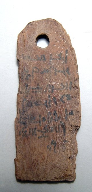 An Egyptian wood tag for a mummy with Demotic text: An Egyptian wood tag for a mummy with Demotic text, Roman Period, c. 1st - 4th Century AD, the writing in black ink one 6 lines and part of a 7th, holed at the top for suspension. 4 1/4" x 1 3/4" (10.