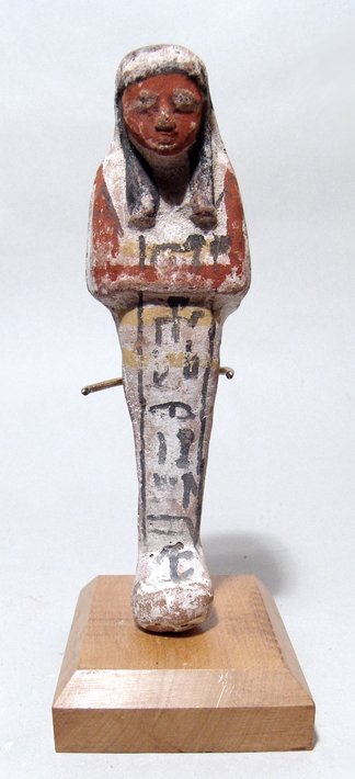 Egyptian terracotta ushabti, New Kingdom: An Egyptian terracotta ushabti, New Kingdom, c. 1570 - 1075 BC, mummiform, wearing tripartite wig with curled locks, arms folded across chest, hands holding pick and hoe, basket at center of back. The