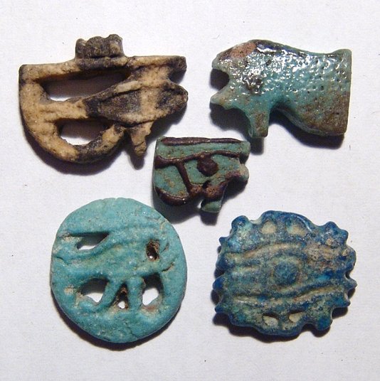 A lot of 5 faience Eye of Horus amulets: A lot of 5 faience Eye of Horus amulets. Lot includes a pair of 3rd intermediate bi-color types, c. 1075 - 945 BC, (L: 1.8 & 1.2 cm), and a 3rd Intermediate yellow faience open-work type, (L: 2.2 cm).