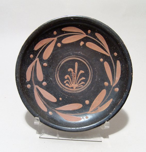An attractive Apulian Xenon-ware plate: An attractive Apulian Xenon-ware plate, Magnia Graecia, c. 350 - 330 BC, with a central palmette with a double ring border within a laurel-wreath, another laurel-wreath below the rim. At the center of