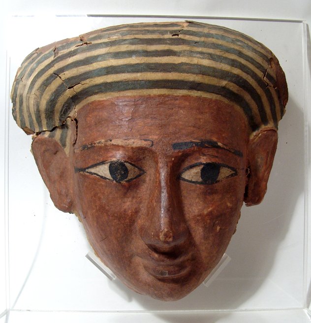 Large Egyptian wood sarcophagus mask: A large and attractive Egyptian wood sarcophagus mask, Late Period, c. 700 - 30 BC, wearing a striped wig, the brownish-red face with handsome features, the eyes wide and detailed with black cosmetic 