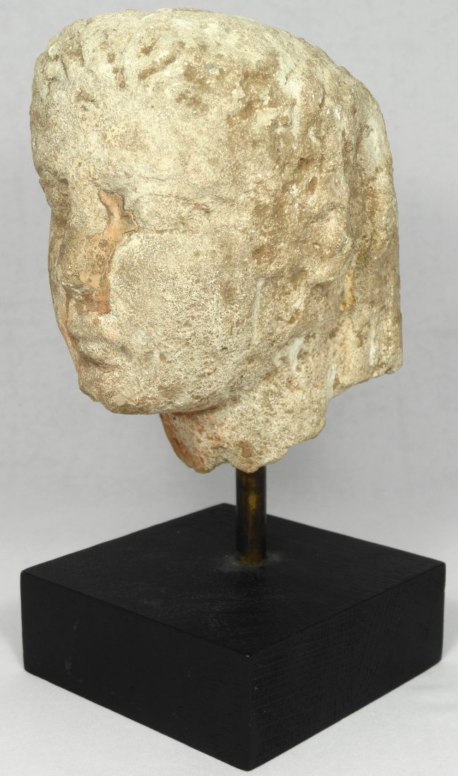 A Greek limestone head of a kouros: A Greek limestone head of a kouros, Archaic, circa 500 B.C. The wavy hair falling down the back of the neck, the face with large almond eyes and a small mouth, some pink skin-coloured slip remaining,