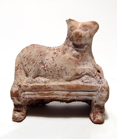 Roman terracotta figure of a Sothic dog: An attractive Roman terracotta figure of a Sothic dog, c. 1st - 2nd Century AD, resting on a low bench. Modeled in the round, head facing with tail to the right front. The dog wears a collar with a ci