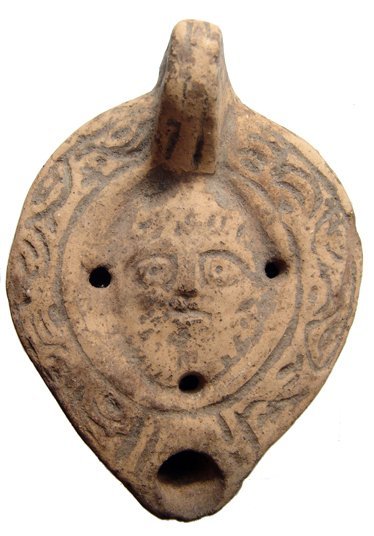 An interesting Roman terracotta lamp from Egypt: An interesting Roman terracotta lamp from Egypt, c. 2nd Century, with frontal bearded male face within the discus, a floral motif around the shoulder, maker's mark 'A ' within concentric circles on ba