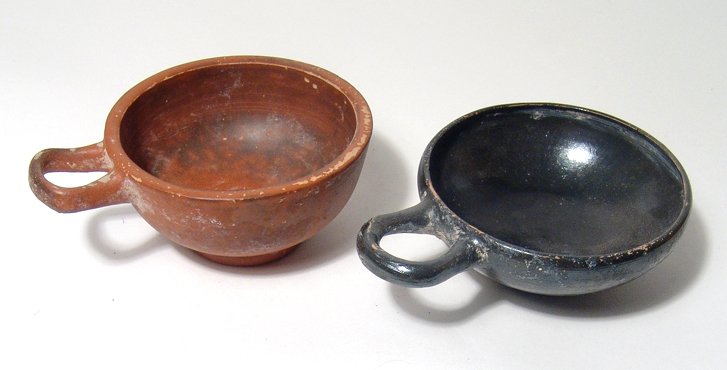 A lot of 2 Greek drinking cups: A lot of 2 Greek drinking cups, Magnia Graecia, c. 4th - 3rd Century BC, one in red-ware and the other with glossy black glaze, both with a single loop handle and raised foot. Red-ware: 4 ¾ in (12.1 