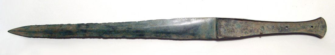 A Near Eastern bronze dagger or short sword: A Near Eastern bronze dagger or short sword, c. 1200 - 1000 BC, the blade and hilt cast as one piece. The blade is long and very slender with wide midrib also tapering with blade. The flanged hilt whi
