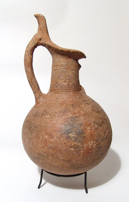 A Cypriot Red Polished Ware Jug: A Cypriot Red Polished Ware Jug, Early Cypriot III - Middle Cypriot I, c. 1900 - 1650 BC, the body round with cylindrical neck, a loop handle attaches from the shoulder to the tall thumb rest protrudi