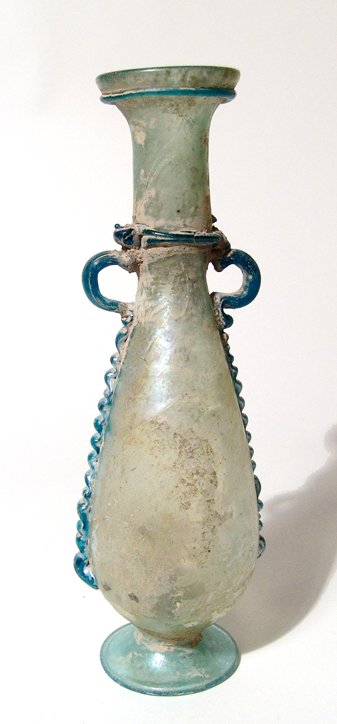 A tall Roman bi-color glass bottle: A tall Roman bi-color glass bottle, c. 4th - 5th Century AD, the body pear-shaped with raised disk foot, tubular neck with slight constriction at base and a flared mouth. On either side are loop handl