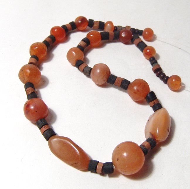 Strand of 17 Near Eastern polished carnelian beads: A strand of 17 Near Eastern polished carnelian beads, c. 1st Millennium BC, of spherical shape, two elongated, all strung together with modern accent beads. L: 13 in (17.7 cm). Ex Los Angeles private