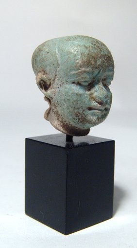 Egyptian turquoise glazed faience head of Pataikos: An Egyptian turquoise glazed faience head of Pataikos, Late Period, c. 664 - 30 BC, well-detailed with nice color. H: 1 1/8 in (2.8cm). Mounted on stand. Ex property of a Bedfordshire, England private