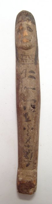 An Egyptian carved wood Peg ushabti: An Egyptian carved wood Peg ushabti, New Kingdom, c. 1570 - 1075 BC, with simplistic features with black wig, cosmetic details and text down front. H: 7 3/8 in (18.8 cm). Intact, some age splitting an