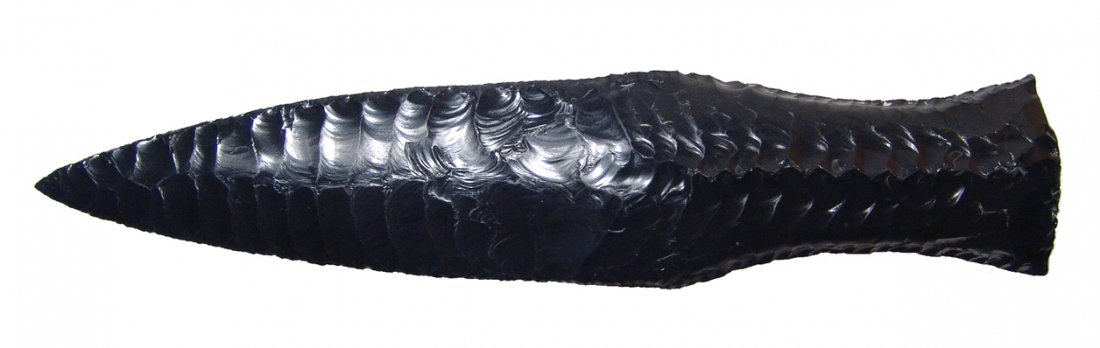 A choice flaked obsidian knife: A choice flaked obsidian knife, in ancient-style, the blade beautifully fashioned with serrated edges and thick handle with central ridge on one side. A marvelous example of the flint-knapper's craft.