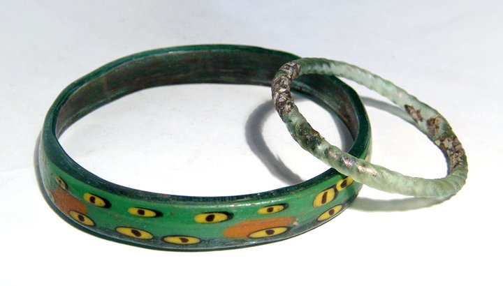 A pair of gorgeous Roman and Islamic glass bracelets: A pair of gorgeous Roman and Islamic glass bracelets. The larger, from the Holy Land, c. 12th - 15th Century AD, in vibrant green glass with the traditional ‘evil’ eye in two rows, each in yellow 