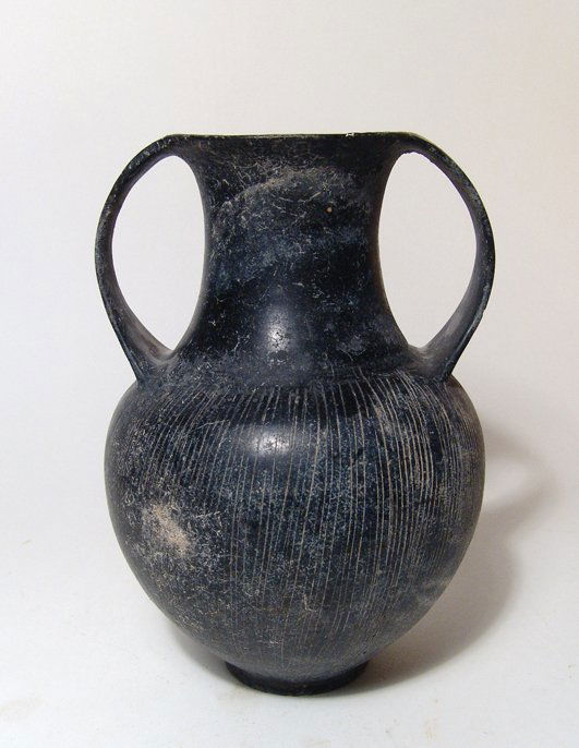 A large Etruscan Bucchero Amphora, Italic: A large Etruscan Bucchero Amphora, Italic, c. 630 - 600 BC, the body with incised vertical lines and narrow disk foot, the neck waisted with two curved flat handles. H: 7 ½ in (19.2cm). Ex South Germ