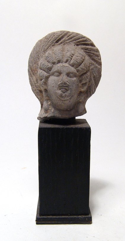 Egyptian grey terracotta head of a woman: An Egyptian grey terracotta head of a woman, Ptolemaic, c. 2nd - 1st Century BC, with full face and wearing a tall diadem, her hair stylized in tight waves into a coiled plait at the back of her head.