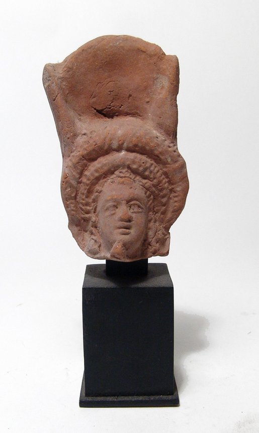 Egyptian terracotta head of Isis: An Egyptian terracotta head of Isis, Roman Period, c. 1st Century BC, wearing a large rolled diadem and headdress consisting of ram’s horn, the diadem taking the place of the usual solar disk. Her f