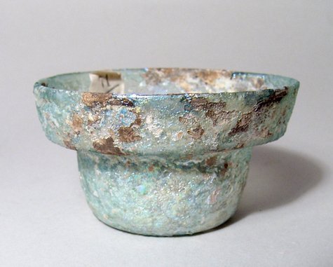 A Roman green glass stepped cup: A Roman green glass stepped cup, c. 2nd - 3rd Century AD, with flattened base and near vertical rim. H: 5.5cm, D: 9.9 cm. Intact with attractive iridescence. Ex collection of Field Marshal Earl Kitche