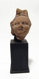 An Egyptian terracotta head of Harpokrates: An Egyptian terracotta head of Harpokrates, Ptolemaic, c. 3rd - 1st Century BC, his features nicely modeled and wearing plumed headdress. Head alone 2 1/4 in (5.7 cm). Removable wood base. Ex