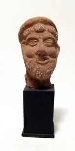 Egyptian terracotta head of a bearded man: An Egyptian terracotta head of a bearded man, Roman Period, c. 1st - 3rd Century AD, perhaps Zeus, wearing a low diadem, his features nicely detailed. H: 3 in (7.6 cm). Custom stand. Ex Philadelphia