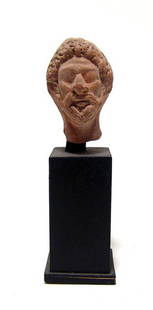 An Egyptian terracotta head of a priest: An Egyptian terracotta head of a priest, Roman Period, c. 1st - 3rd Century AD, wearing leopard-skin hood, beard and mustache. H: 1 3/4 in (4.4 cm). Custom stand. Ex Philadelphia private collection.