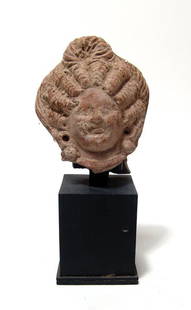 An Egyptian terracotta head of a woman: An Egyptian terracotta head of a woman, Roman Period, c. 1st - 3rd Century AD, wearing a large diadem, her hair styled in thick waves with a plait atop her head, her features pleasant and the ears