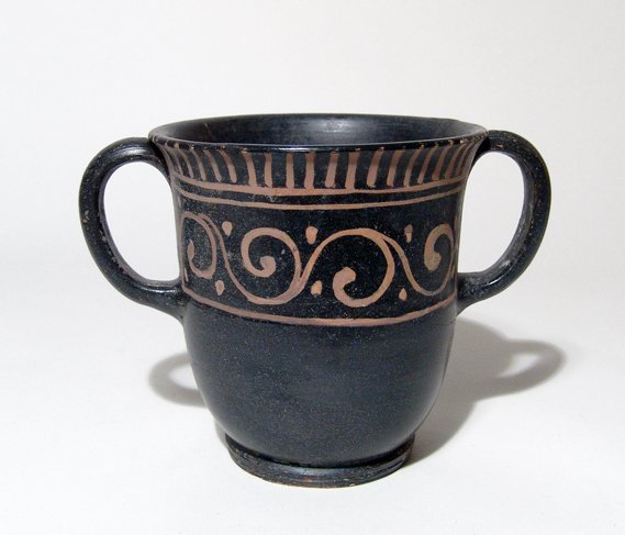 A very nice Greek handled cup: A very nice Greek handled cup, Magnia Graecia, c. 4th Century BC, the tall body beautifully decorated with a floral band in a deep orange slip, vertical tongues just below the rim. H: 4 1/2 in (11.6 c