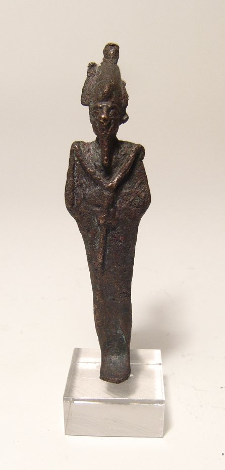 An Egyptian bronze figure of Osiris: An Egyptian bronze figure of Osiris, Late Period, c. 664 - 30 BC, mummiform, wearing atef crown with uraeus and false beard, arms folded across chest, hands holding a crook and flail. H: 3 1/2 in (8.9