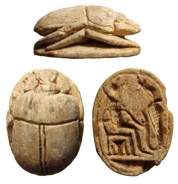 Egyptian steatite scarab, New Kingdom: A nice Egyptian steatite scarab, New Kingdom, c. 1570 - 1075 BC, with well-formed body and legs, on base, a seated deity holding a uraeus by the tail. 15 x 11mm. Ex Los Angeles private collection.