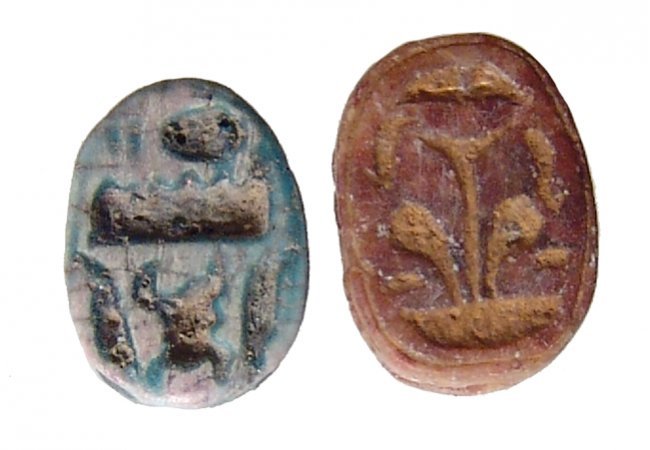 A lot of 2 Egyptian steatite scarabs, New Kingdom: A lot of 2 Egyptian steatite scarabs, New Kingdom, c. 1570 – 1075 BC, both with nicely carved bodies, the first in a reddish steatite with a lotus plant on the reverse, 12 x 9mm, the second with the