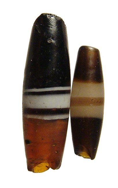 A pair of lovely Roman glass beads, Egypt: A pair of lovely Roman glass beads, Egypt, c. 3rd Century AD, each with tapered ends and in a root beer colored glass with center white banding. Larger with half translucent and half opaque. L: 29mm &