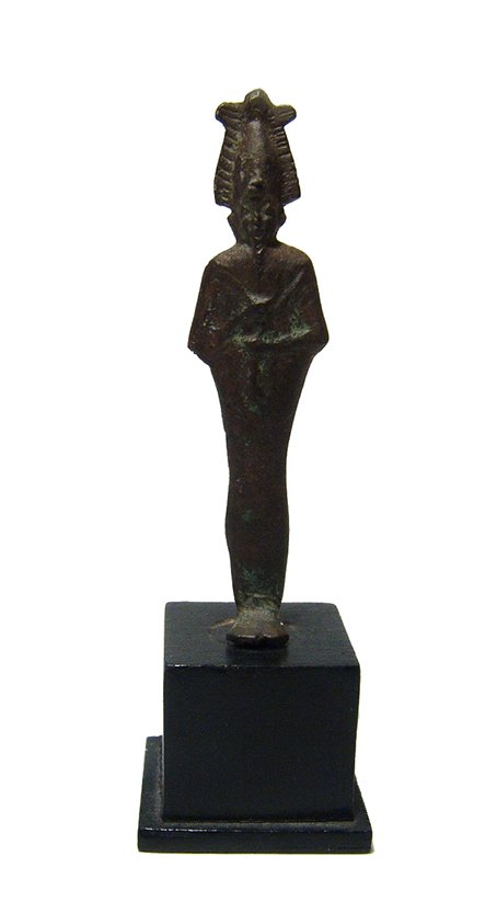 An Egyptian bronze votive figure of Osiris: An Egyptian bronze votive figure of Osiris, Late Period, c. 664 – 30 BC, depicted mummiform, wearing Atef crown with uraeus and false beard, arms folded at chest, hands grasping a crook and a flail.