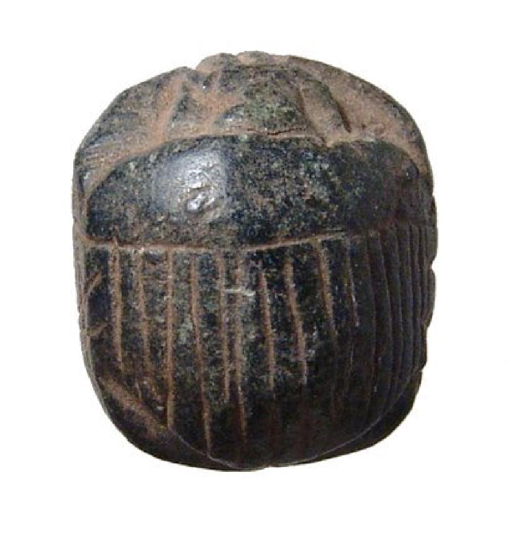 An Egyptian black steatite scarab, Late Period: An Egyptian black steatite scarab, Late Period, c. 664 - 332 BC, with striated clypeus similar to larger heart scarabs, the base flat, perhaps used as an amulet. 20 x 18mm. Cf. Petrie Amulets, 89d; Ex