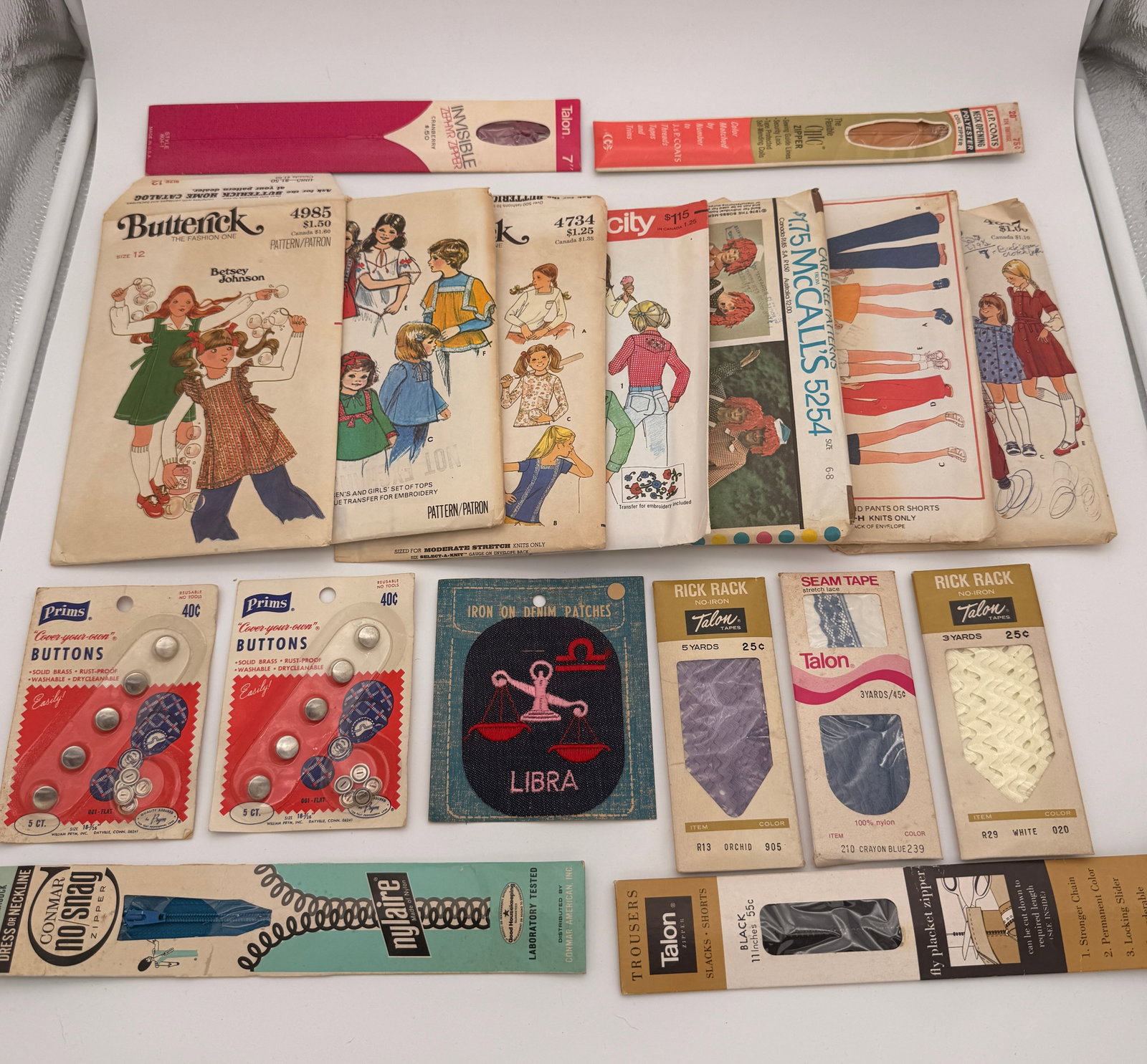 Lot of 17 vintage sewing accessories in original packages: 7 Butterick Patterns / 2 Prims Buttons packages / 2 Rick Rack Talon Tapes / 1 Seam Tape Talon Tape / 1 Iron On Denim Patch / 4 Zipper Tape Trims