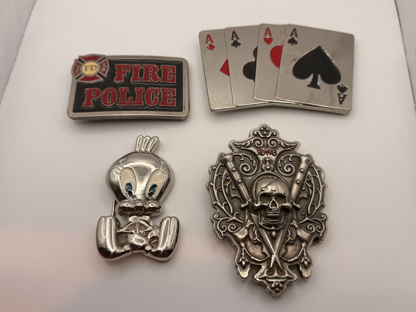 Lot of Four Vintage Novelty Belt Buckles: Group of four vintage belt buckles including Fire Police, Four Aces poker hand, character figure, and skull with crossed rifles motif. Cast metal construction, mixed finishes.