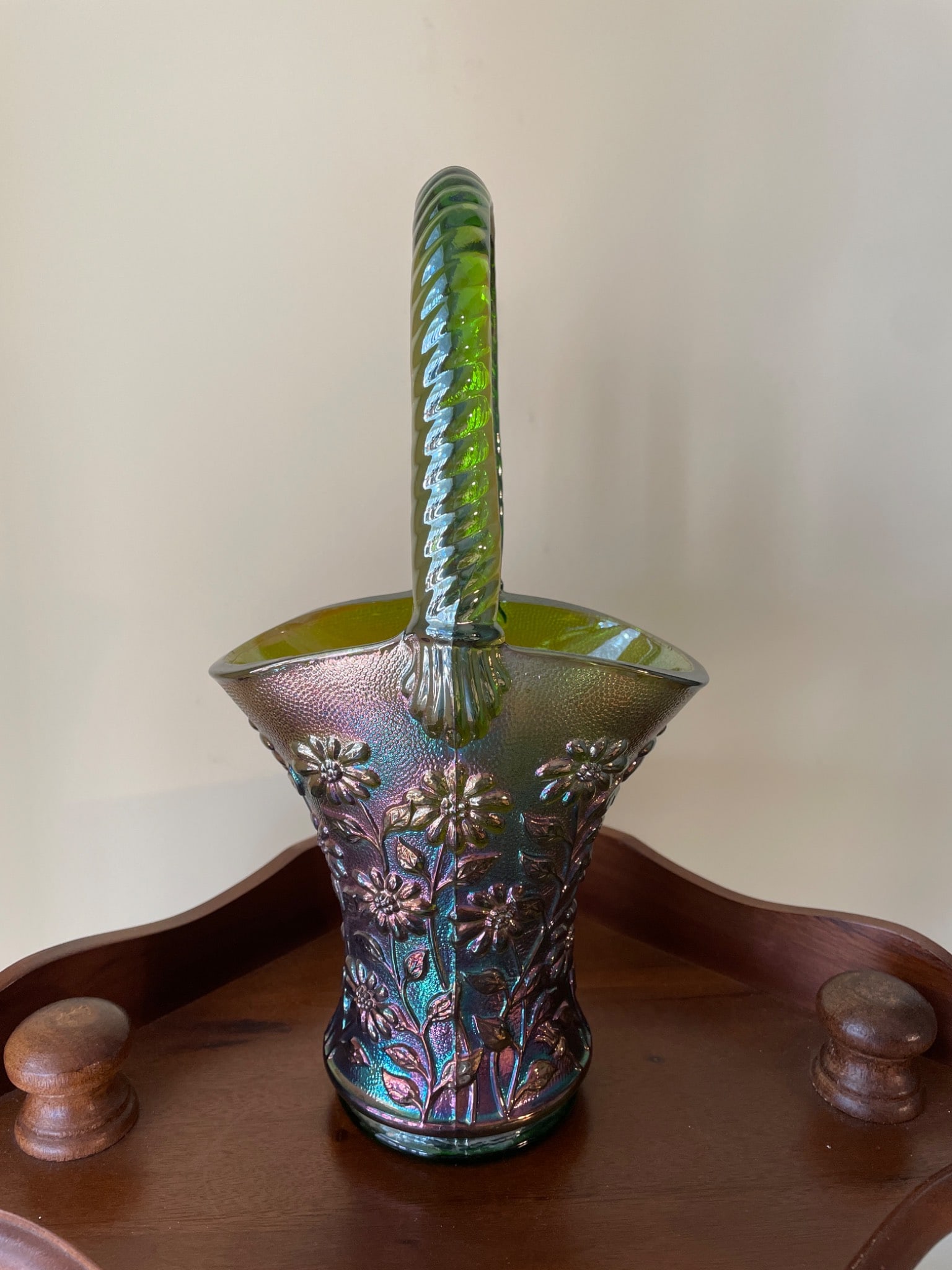 Green Iridescent Glass Basket with Floral Motif and Twisted Handle: This item is a green translucent glass basket featuring an iridescent finish. The basket includes detailed floral patterns and a twisted handle design. The base of the basket displays a pressed