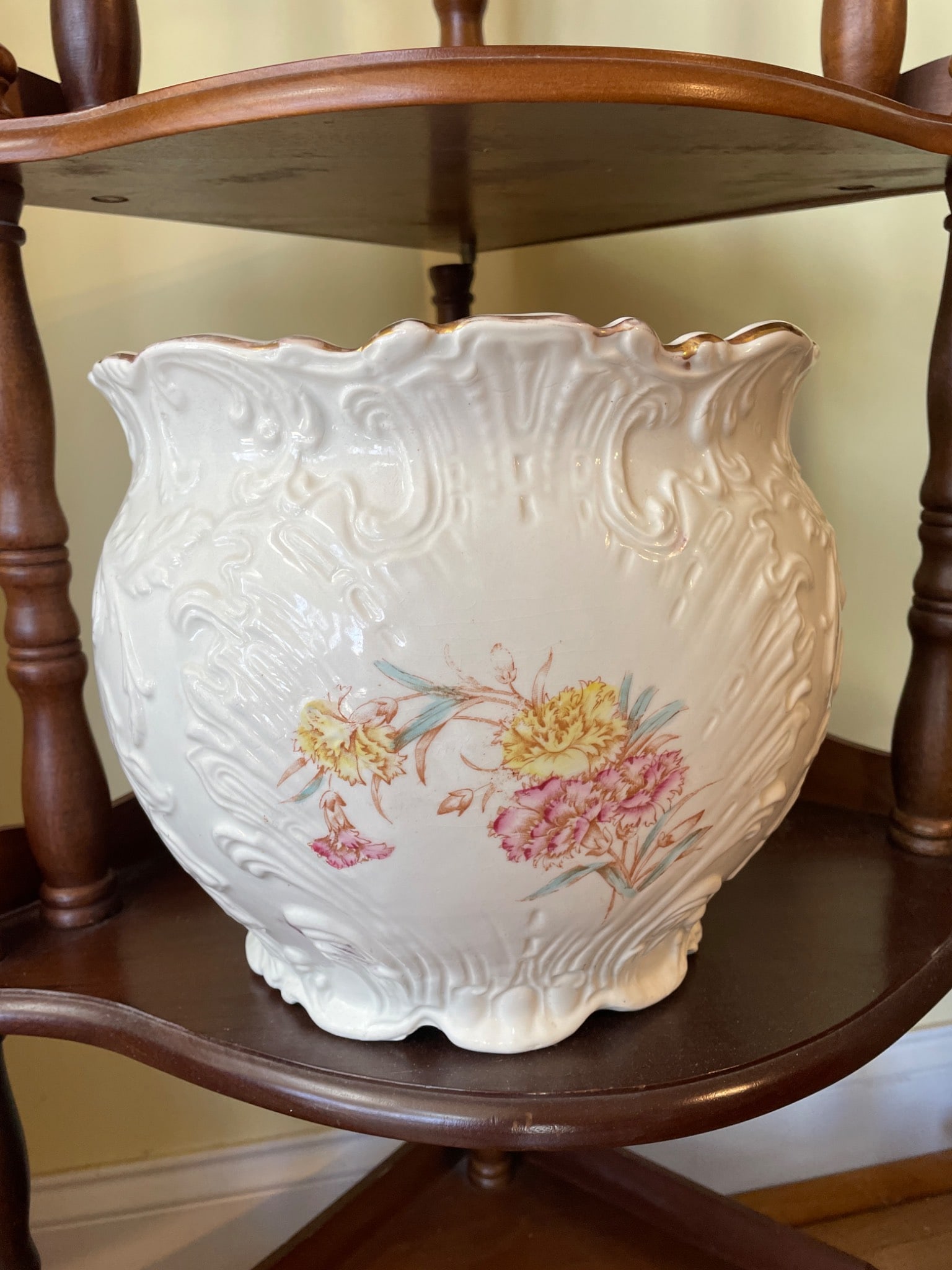 Large White Ceramic Planter With Floral Design and Maker Stamp: This is a large white ceramic planter with a detailed floral design, featuring pink and yellow flowers. The exterior includes an embossed pattern with curved accents. The planter has a gold-toned rim
