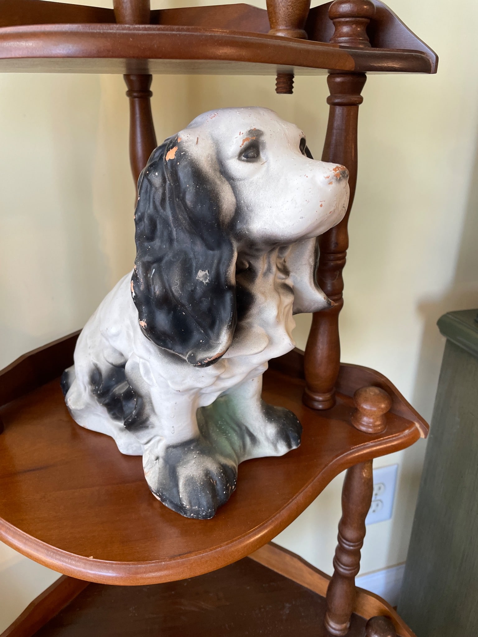 Painted Ceramic Dog Figurine With Black Ears and White Body: This is a painted ceramic dog figurine, featuring a white body with black ears and detailing. The item appears to be hand-painted and displays wear consistent with age. No visible markings or model