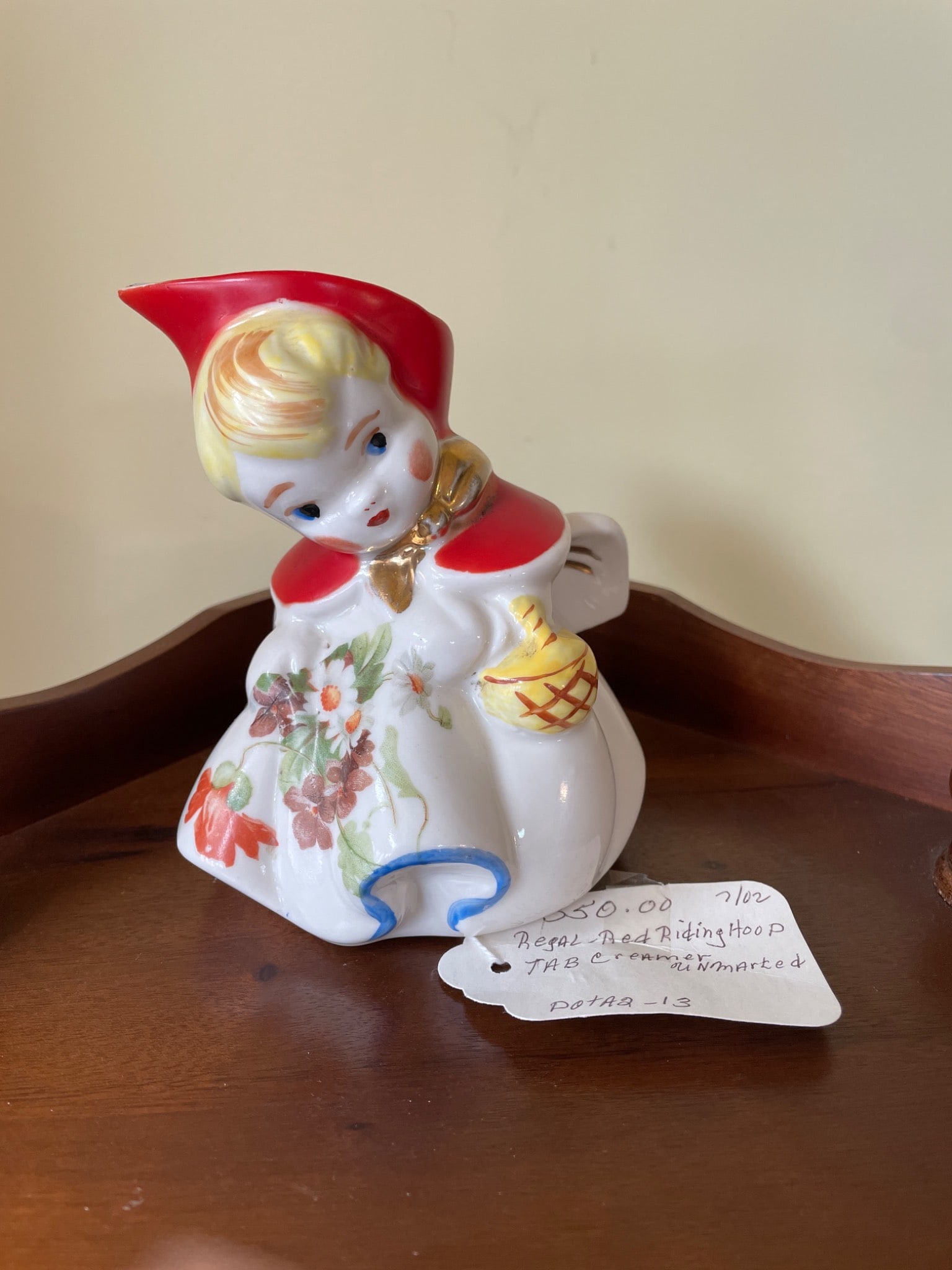 Porcelain Red Riding Hood Creamer, Hand-Painted, Unmarked: This item is a porcelain creamer styled as Red Riding Hood with hand-painted floral and gold accents. It is unmarked and features vibrant colors of red, yellow, and white. Likely mid-20th century
