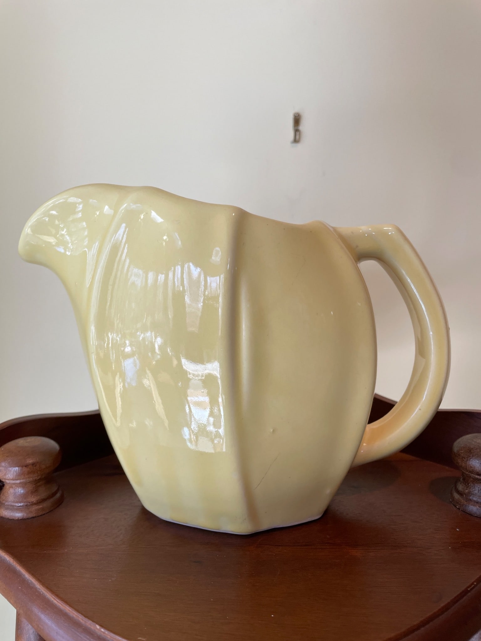 Ceramic Yellow Pitcher with Fluted Design: A ceramic yellow pitcher with a fluted design, featuring a wide spout and an integrated handle. The base is unmarked and glazed. The pitcher shows minor imperfections, including light surface