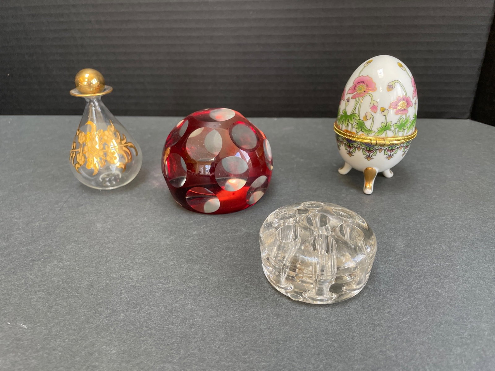 Decorative Glass and Ceramic Objects: This lot includes four items: 1) A clear glass perfume bottle with gold floral detailing and a matching stopper. 2) A red faceted glass paperweight with circular designs. 3) A clear faceted glass