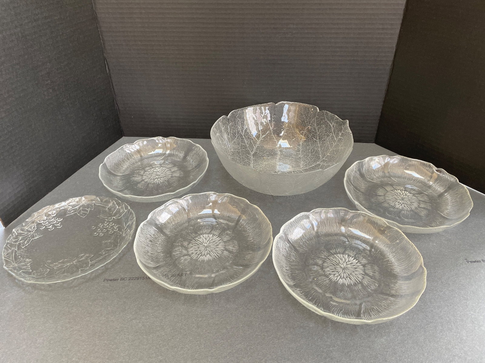 Clear Glass Serving and Salad Bowl Set with Floral Design: This set includes one large serving bowl and five smaller matching salad bowls, all clear glass with an etched floral and leaf pattern. The bowls feature scalloped rims and detailed designs. No visibl