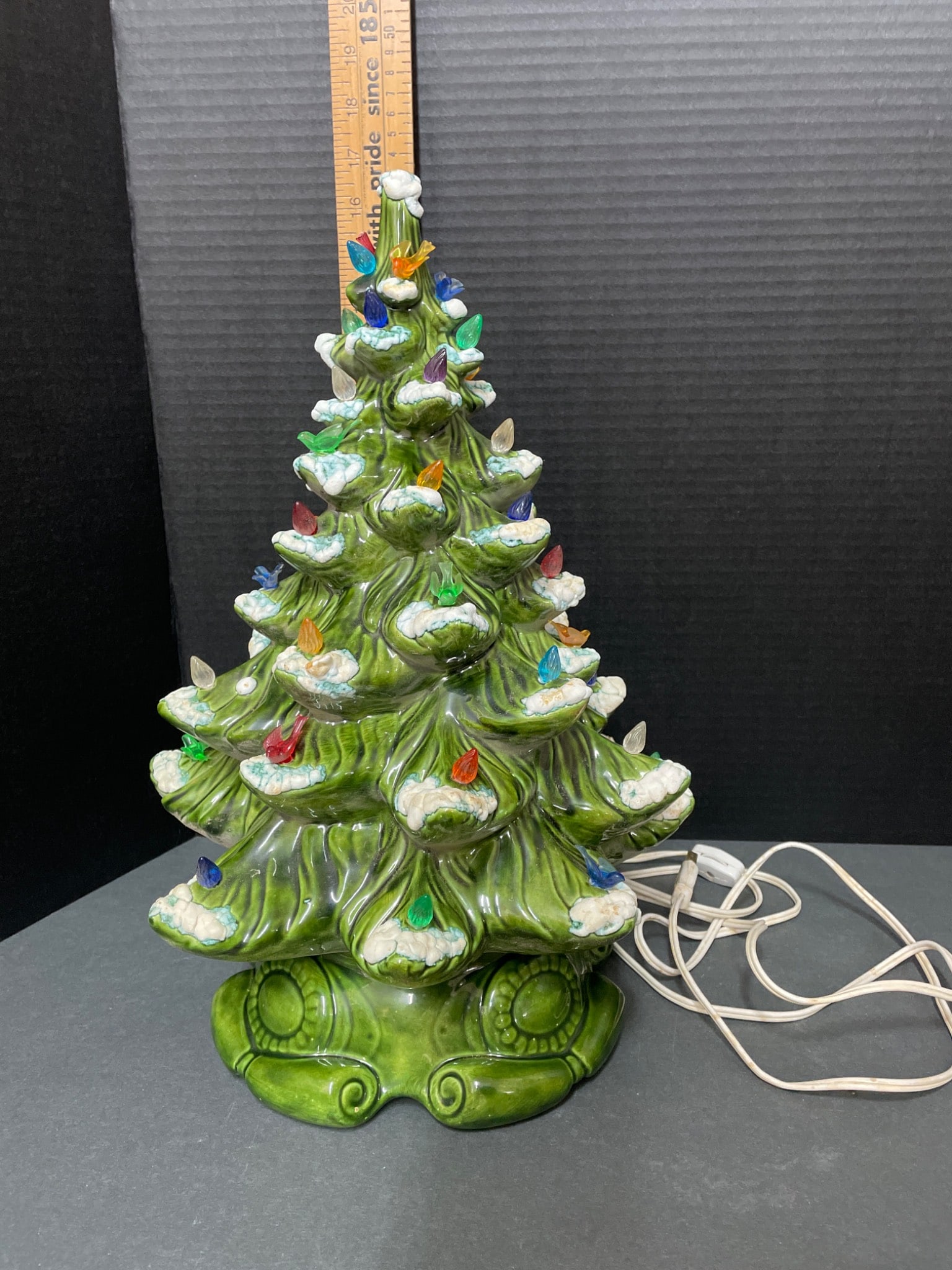 16-Inch Tall Ceramic Christmas Tree With Multicolored Bulbs and Base: A 16-inch tall ceramic Christmas tree featuring multicolored plastic bulb accents on snow-dusted branches. Mounted on a detachable green ceramic base with an integrated electrical socket and cord for