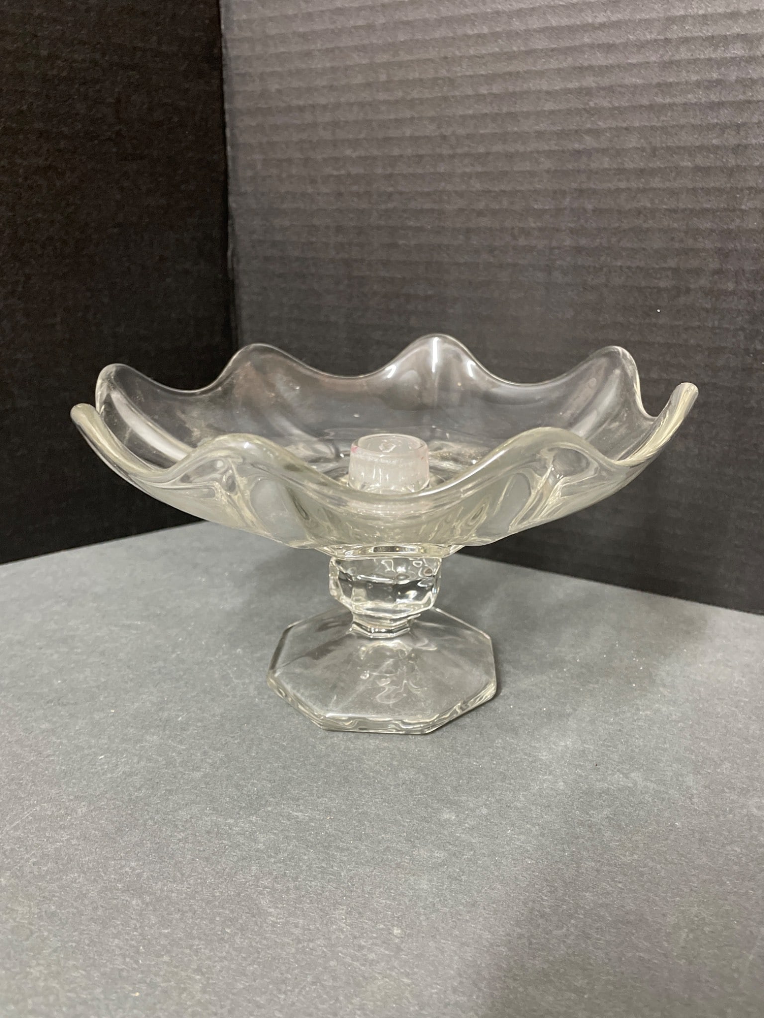 Clear Glass Compote with Wavy Rim and Octagonal Base: This is a clear glass compote featuring a wavy rim design and an octagonal base. The estimated height is approximately 6 inches, as shown in the photo with a ruler for scale. The piece has a center