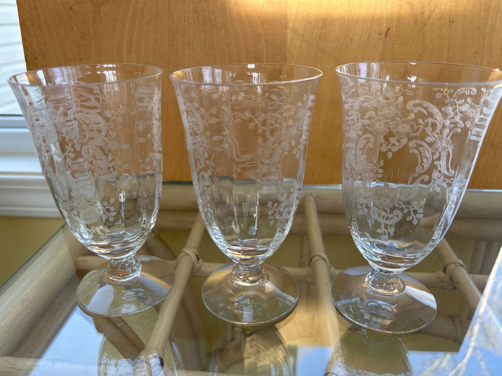 Three Clear Glass Stemmed Goblets with Etched Floral Patterning: Three clear glass stemmed goblets featuring detailed etched floral patterns. All three goblets are uniform in appearance and design, and their bases are circular with a flat foot. The glasses show no